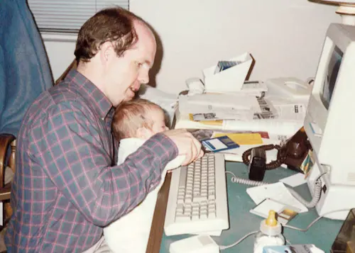 Matt’s father holding him in his lap as an infant typing on a Macintosh SE